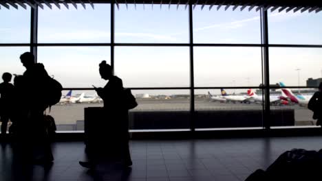 Silhouettes-of-tourists-walking-by-huge-terminal-window,-passengers-at-airport