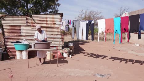 Afrikanische-Frau-ohne-fließendes-Wasser,-Wäsche-in-einem-Eimer-vor-ihrem-Hause-Blechhütte