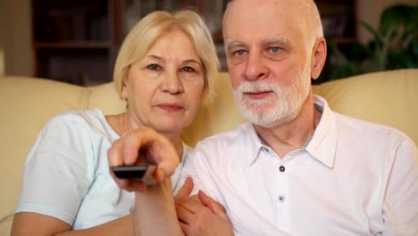 Senior-pareja-relajante-en-el-sofá-en-casa-viendo-la-televisión.-Jubilados-ver-canales-con-control-remoto