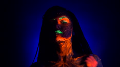 Sexy-Mädchen-schmiert-und-fluoreszierende-Farbe-auf-ihrem-Körper-reibt.-Farbstoff-unter-UV-Schwarzlicht-Leuchten.-Frau-mit-Zöpfen-im-Neonlicht.-Night-Club,-Party,-Halloween-psychedelischen-Konzepte