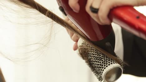 Hairstylist-using-dryer-for-drying-long-hair-and-hairbrush-for-styling-after-hairdressing-in-beauty-studio.-Close-up-hairdresser-making-hairstyling-in-hairdressing-salon