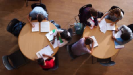 Tiro-arriba-Defocused-de-alta-alumnos-en-grupo-de-estudio-alrededor-de-mesa