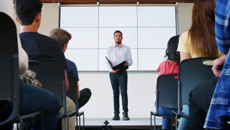 Profesor-dando-presentación-a-clase-de-la-High-School-secundaria-frente-a-pantalla