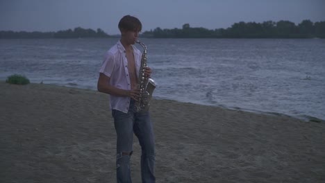 Chico-joven-guapo-es-jugar-el-saxophone-en-la-orilla-del-río