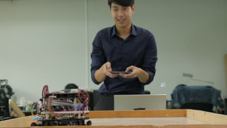 Electronics-engineer-programming-and-control-robots-to-playing-soccer-with-mobile-phone-in-the-workshop.-People-with-technology-or-innovation-concept.