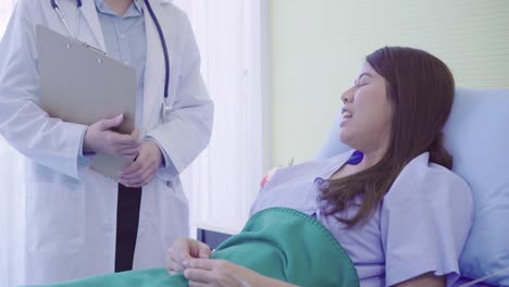 Beautiful-smart-Asian-doctor-and-patient-discussing-and-explaining-something-with-clipboard-in-doctor-hands-while-staying-on-Patient's-bed-at-hospital.-Medicine-and-health-care-concept.