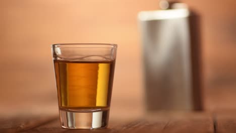 Enfoque-pull-de-un-vaso-de-whisky-un-disparo-a-un-matraz-de-cadera-metálico-en-el-fondo