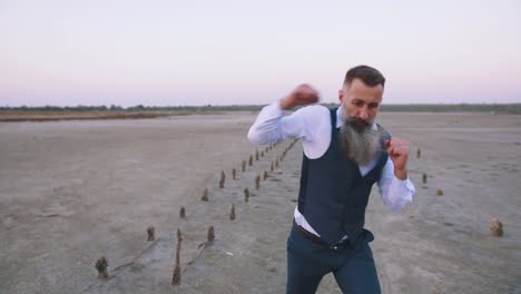 Mature-handwome-man-in-suit-with-long-gray-beard-boxing-with-shadow-outdoors-on-beach,-slow-motion