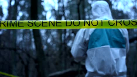 Field-forensic-expert-working-with-evidence-on-site,-yellow-crime-scene-tape