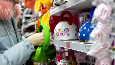 A-young-woman-chooses-a-green-steel-kettle-in-the-supermarket.