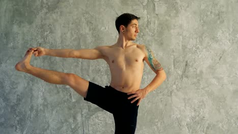 Männliche-Yogameister-Dehnung-Bein-im-Studio.-Stehend,-ein-Bein-in-der-Hand-halten