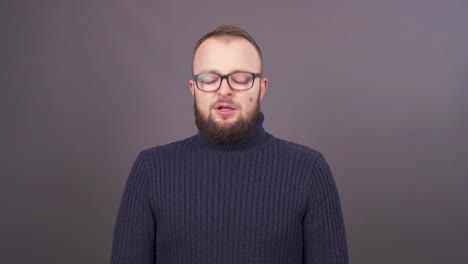 Close-up-portrait-of-a-bearded-young-snotty-caucasian-man-in-glasses-,-sneezing-and-blowing-his-nose.-Isolated-on-grey-background.