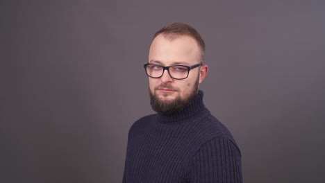 Close-up-portrait-of-profile-young-beard-man-in-glasses.-Unexpected-ironic-laughing-at-camera.-Isolated-on-grey-background.