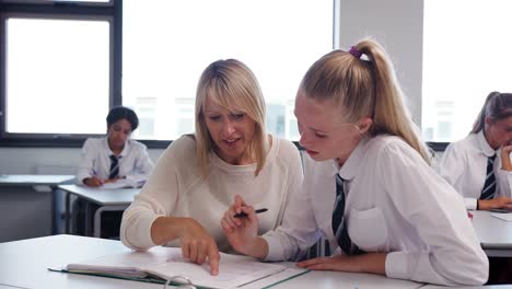 High-School-Lehrer-geben-uniformierten-Studentin-Einzelunterricht-am-Schreibtisch-im-Klassenzimmer