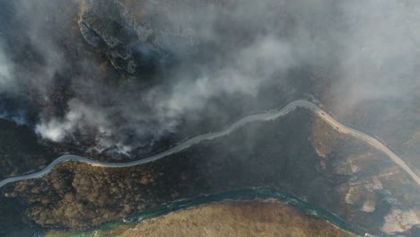 Vertikale-Luftaufnahmen-von-Wald-bedeckt,-in-dichten-Rauch,-eine-Straße-und-einen-Fluss-in-der-Nähe-von