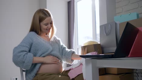 modern-pregnancy,-maternity-woman-with-naked-belly-considering-new-clothes-for-future-child-bought-on-Internet-sitting-in-front-of-computer