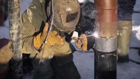 Worker-produces-pipe-welding-on-the-street.-In-winter,-at-low-temperatures,-it-is-difficult-to-mount-the-pipe-wire