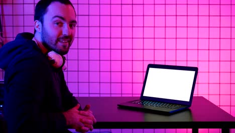 A-young-cheerful-gamer-smiling-to-the-camera-and-looking-at-laptop.-White-Display