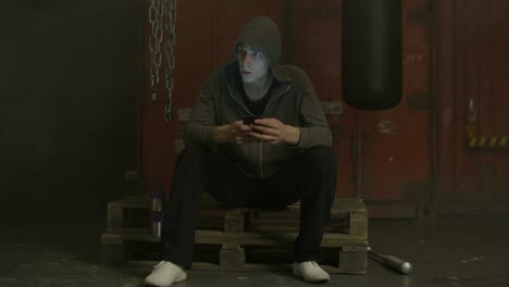 Grim-man-in-hoodie-text-messaging-on-cellphone