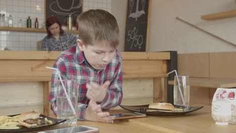 Kleine-Junge-spielen-am-Telefon,-während-sie-im-Café-essen