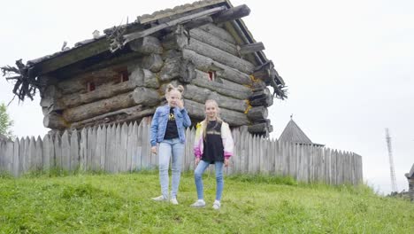 Zwei-Mädchen-Teenager-stehen-auf-grünem-Rasen-auf-rotierenden-Märchenhaus.-Teenager-Mädchen-posiert-auf-Holzhaus-der-alten-Hexe-im-Märchendorf