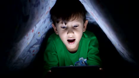Little-boy-reading-book-on-digital-tablet-at-night