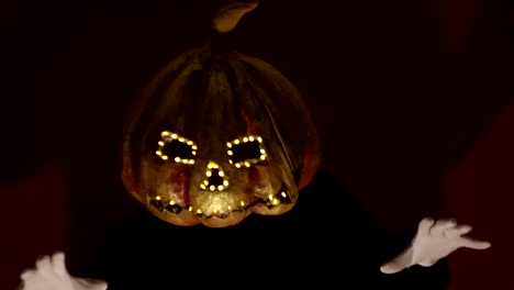 Scary-man-with-a-pumpkin-head-and-luminous-eyes-looks-at-the-camera.-Man-with-a-pumpkin-head-scares-raising-his-hands-up.-Halloween.