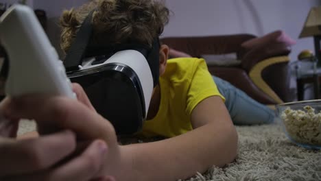 Close-up-portrait-of-teenage-Caucasian-boy-laying-on-the-floor-wearing-VR-headset-and-holding-remote-control.-Child-playing-virtual-reality-game.-Generation-Z,-gaming.-Cinema-4k-ProRes-HQ.