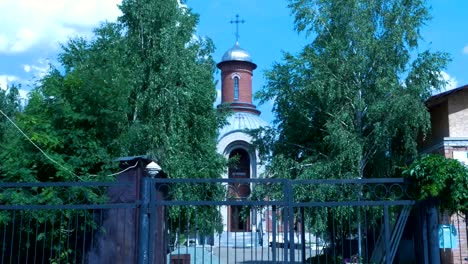 Ladrillo-del-templo-ortodoxo-naranja-con-sunny-ray,-floración-verdes-árboles-en-primer-plano.-Nubes-blancas-del-cielo-azul.-Orar:-Santa-Iglesia-de-Cristo-nueva-luz.-Tiempo-de-verano,-día-soleado