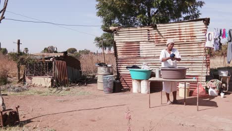 Afrikanische-Frau-ohne-fließendes-Wasser,-Wäsche-in-einem-Eimer-vor-ihrem-Hause-Blechhütte