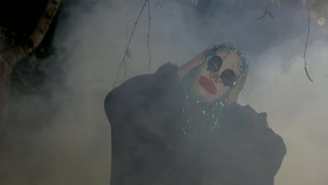 Malefic-halloween-funny-clown-wearing-a-mask-and-green-fake-hair-performing-an-evil-dance-in-a-dark-forest