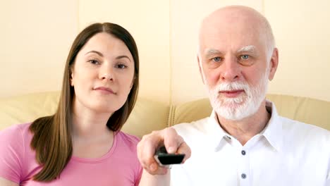 Father-and-daughter-relaxing-on-sofa-at-home-watching-TV.-Switching-channels-with-remote-control