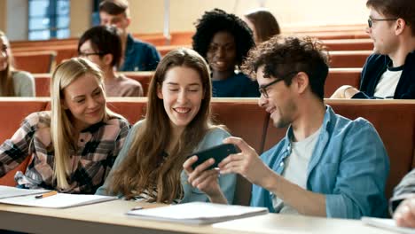 Männliche-Schüler-Aktien-Handy-Bildschirm-mit-anderen-Studenten,-sie-Lächeln.-Scherz-in-der-Universität-Klasse.