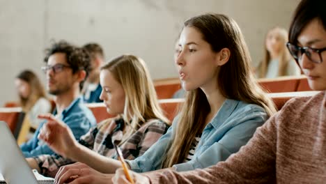 Schöne-junge-Student-nutzt-Laptop-beim-Hören-eines-Vortrags-an-der-Universität,-sie-wirft-Hand-und-fragt-Dozent-einer-Frage.-Multi-ethnischen-Gruppe-von-modernen-hellen-Studenten.