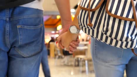 Young-couple-holding-hands-of-each-other-and-walking-at-terminal-of-airport.-Man-and-woman-taking-arms-and-stepping-during-trip.-Symbol-of-love-and-devotion.-Close-up-Rear-back-view