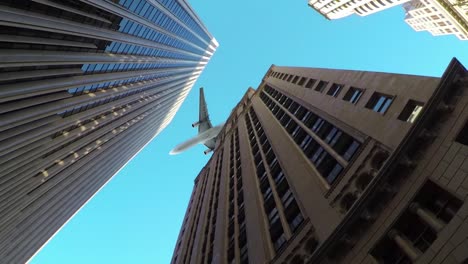 BOTTOM-UP:-Modern-airplane-flies-over-towering-skyscrapers-in-metropolitan-city.