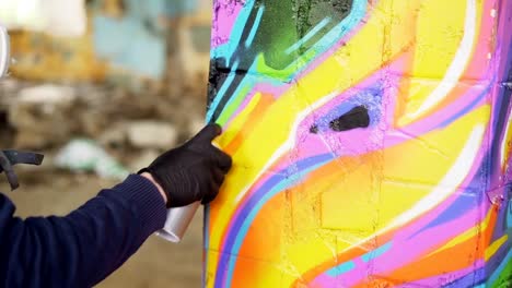 Close-up-shot-of-male-hand-in-leather-glove-holding-spray-paint-and-painting-graffiti-on-old-pillar-inside-abandoned-building.-Modern-art,-abstract-images-and-people-concept.