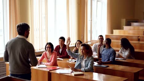 Freundlich-fröhlich-Lehrer-bärtigen-Mann-stellt-Fragen-wissen-überprüfen,-während-Studenten-Hände-erhebend-sind-und-Beantwortung,-junge-Menschen-glücklich,-sind-Wenn-richtige-Antwort-gibt.