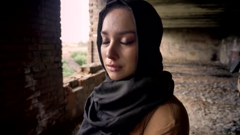 Portrait-of-young-sad-muslim-woman-in-hijab-crying,-armed-soldier-walking,-abandoned-building-background,-military-concept