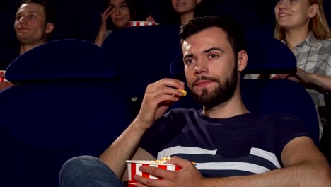 Attraktive-junge-Mann-isst-Popcorn-während-langweiligen-Film-im-Kino