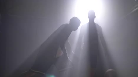 Two-basketball-players-silhouette-playing-one-on-one-in-room-with-smoke-and-floodlit