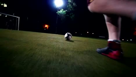 Player-in-black-and-red-sneakers-runs-up-to-the-ball-and-makes-a-kick-towards-the-goal,-but-the-goalkeeper-beats-the-ball,-green-grass,-night-shooting