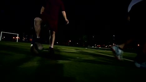 Player-in-white-sneakers-makes-the-transfer-of-the-ball-to-another-player-who-runs-with-the-ball-and-breaks-away-from-other-players,-night-shooting,-on-the-green-grass