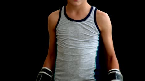 A-teenager-stands-in-boxing-gloves-on-a-dark-background.-The-boy-has-black-and-white-gloves-that-almost-cover-his-face.-The-boy-is-dressed-in-a-gray-jersey,-has-blond-hair-and-dark-eyes
