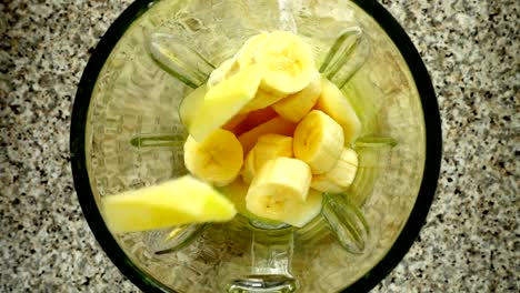 Pieces-of-apples-fall-in-a-blender-bowl-on-pieces-of-bananas.-Slow-motion.	Shooting-in-kitchen.-Top-view.