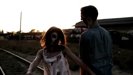 Concepto-película-del-horror-de-Halloween.-Foto-de-creepy-masculinos-y-femeninos-zombies-al-aire-libre,-en-el-ferrocarril.-Brilla-sol-y-pueblo-abandonado-en-el-fondo