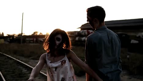 Halloween-horror-filming-concept.-Picture-of-creepy-male-and-female-zombies-outdoors,-standing-on-the-railway.-Abandoned-town-and-sun-shines-on-the-background