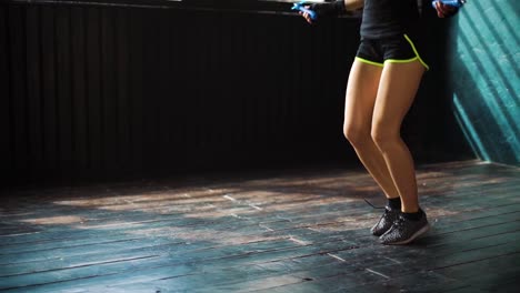 Slow-motion-young-serious-female-boxer-in-wrapped-hands-warming-up,-jumping-on-skipping-rope-in-gym