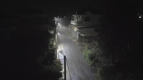 Fuertes-lluvias-durante-la-noche.-Hombre-manejando-una-motocicleta-en-la-pequeña-calle