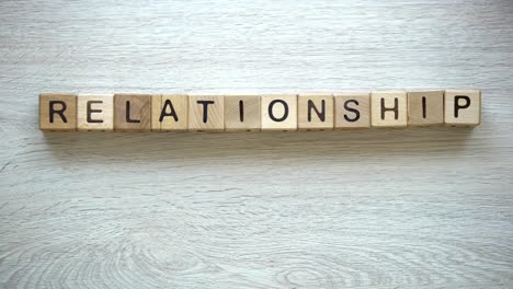 Relationship-word-on-wooden-cubes,-female-hands-tearing-paper-heart-in-half